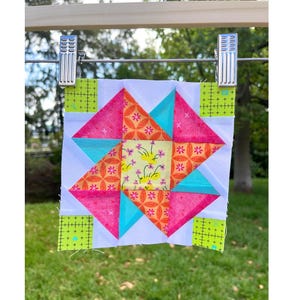 Può includere: Un blocco per trapunta quadrato con un quadrato centrale in tessuto giallo a motivo floreale, circondato da forme geometriche in rosa brillante, arancione e turchese. Gli angoli sono costituiti da quadrati verde lime con segni di griglia neri.