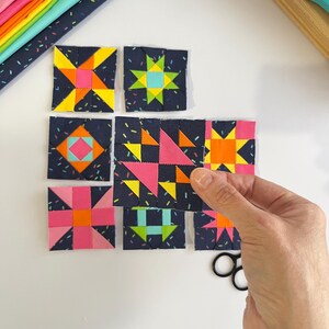 Peut inclure: Un ensemble de huit blocs de courtepointe carr&eacute;s en tissu pr&eacute;sentant des motifs g&eacute;om&eacute;triques rose n&eacute;on, jaune, orange et bleu sarcelle sur un fond bleu marine fonc&eacute; avec un imprim&eacute; confettis, dispos&eacute;s en grille avec un bloc tenu en main.