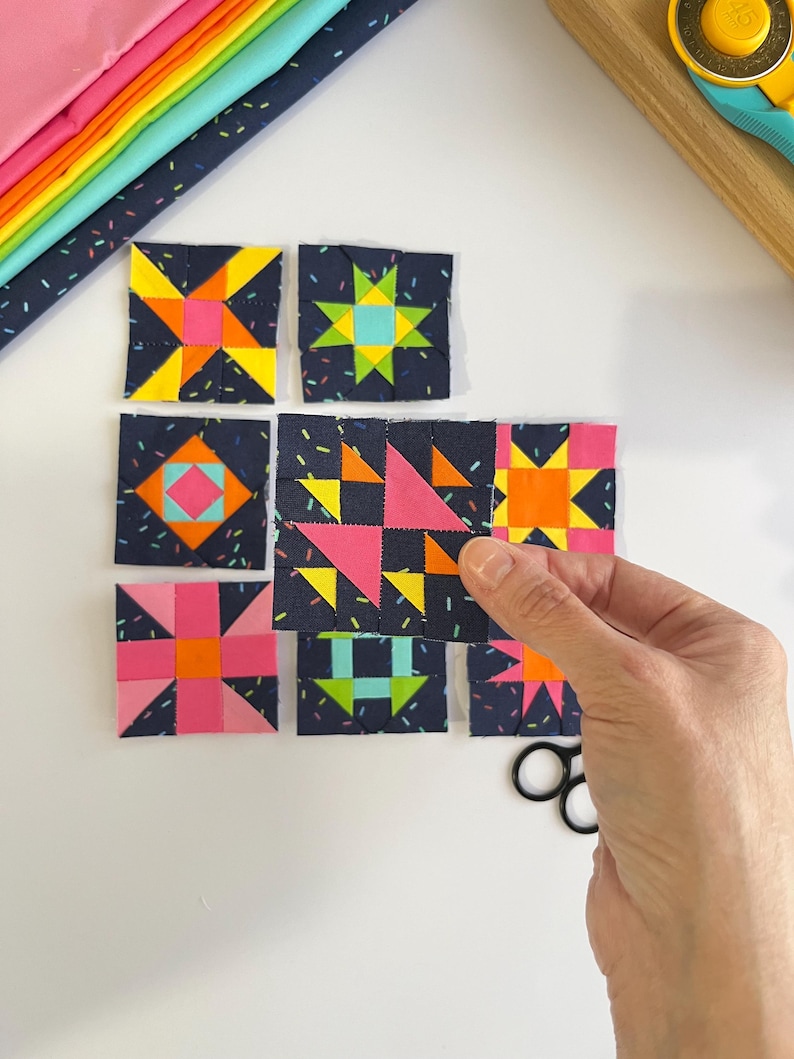 Peut inclure: Un ensemble de huit blocs de courtepointe carr&eacute;s en tissu pr&eacute;sentant des motifs g&eacute;om&eacute;triques rose n&eacute;on, jaune, orange et bleu sarcelle sur un fond bleu marine fonc&eacute; avec un imprim&eacute; confettis, dispos&eacute;s en grille avec un bloc tenu en main.