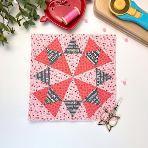 Puede incluir: Un bloque de colcha de retazos rosa y rojo con un diseño de estrella. La tela tiene una variedad de patrones y texto, incluyendo "Sew Good", "Friends", "Love You", "Family" y "To Pi Quilt is by Kindness".