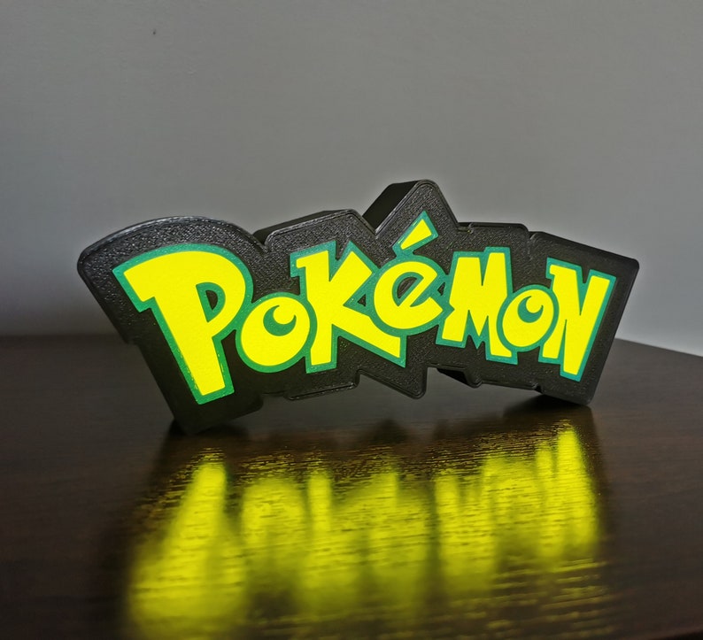 May include: Black and green 3D printed Pok&eacute;mon logo. The logo is made of plastic and has a glossy finish.