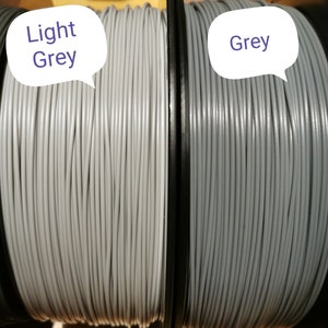 May include: Two spools of filament for 3D printing. The spool on the left is light grey and the spool on the right is grey.