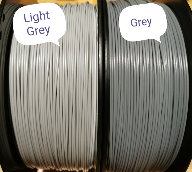May include: Two spools of filament for 3D printing. The spool on the left is light grey and the spool on the right is grey.