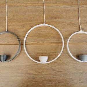 May include: Three hanging planters, two white and one black, with a simple design. Each planter has a small, round, white or gray pot in the center.