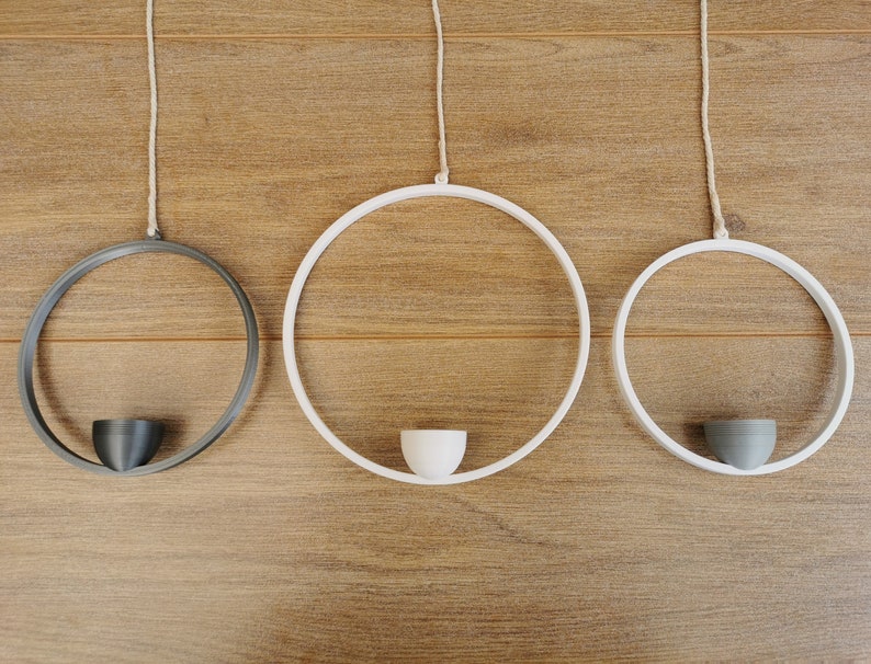 May include: Three hanging planters, two white and one black, with a simple design. Each planter has a small, round, white or gray pot in the center.
