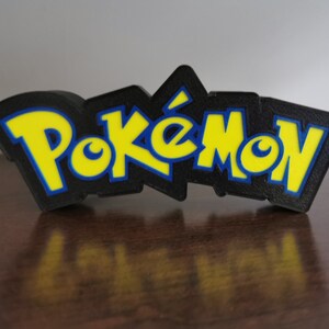 May include: A 3D printed black, yellow, and blue Pok&eacute;mon logo. The logo is raised and has a textured surface.