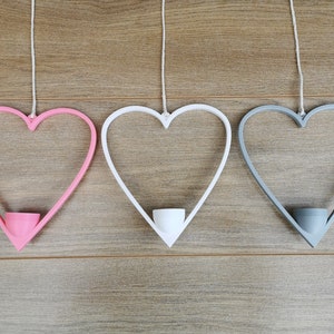 May include: Three heart-shaped hanging planters, one pink, one white, and one gray. Each planter has a small, round opening at the bottom for a plant.