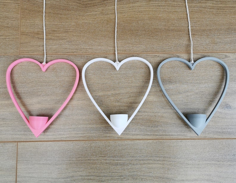May include: Three heart-shaped hanging planters, one pink, one white, and one gray. Each planter has a small, round opening at the bottom for a plant.