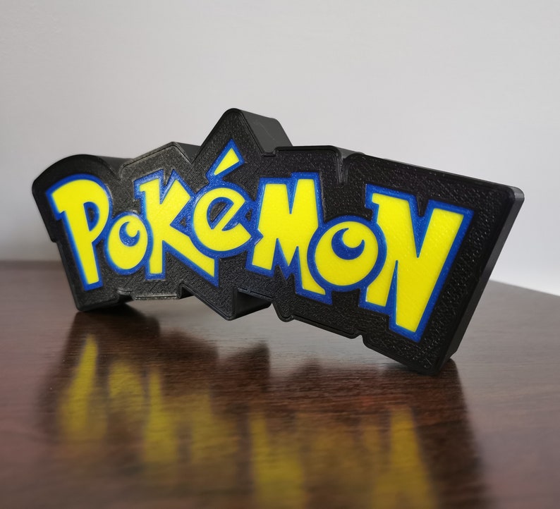 May include: A black 3D printed sign with the word "Pokemon" in yellow and blue letters.