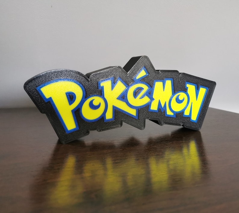 May include: A black 3D printed sign with the word "Pokemon" in yellow letters with blue outlines.