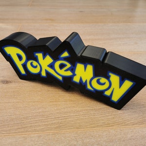 May include: Black 3D printed Pokemon logo with yellow and blue lettering.