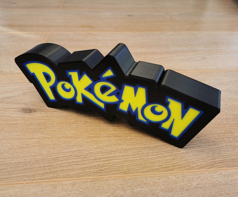 May include: Black 3D printed Pokemon logo with yellow and blue lettering.