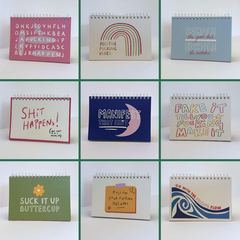 May include: A collection of nine spiral-bound desk calendars with various motivational phrases and designs. The calendars feature colorful text and illustrations, including rainbows, moons, and floral elements. The color palette includes pink, blue, green, and white.