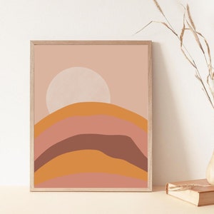 May include: Abstract art print with a pink, orange, and brown color scheme. The print features a large white circle in the center, representing the sun, and a series of curved lines that resemble hills or mountains.