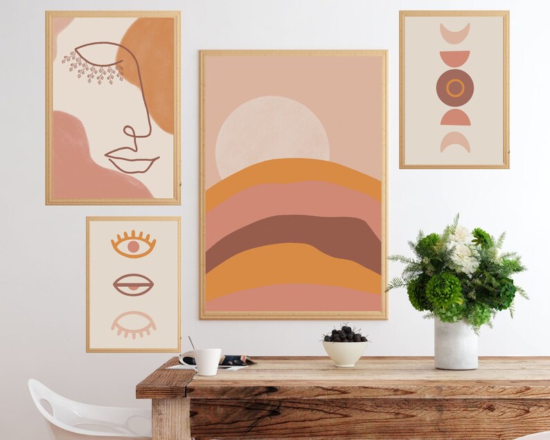 May include: Four framed abstract art prints with a boho aesthetic. The prints feature a line drawing of a face, a sun with a landscape, a series of circles, and a series of eyes. The prints are hung on a white wall above a wooden table with a vase of flowers and a bowl of fruit.