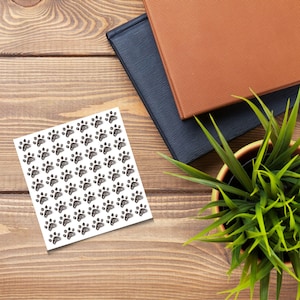 May include: A sheet of white paper with a repeating pattern of black paw prints.