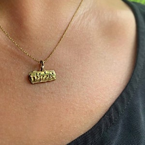 May include: A gold necklace with a pendant featuring Hebrew lettering. The pendant is rectangular and has a textured surface.