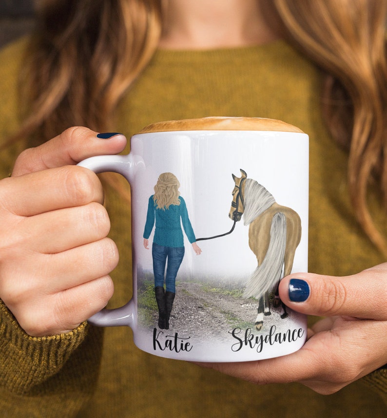 May include: White ceramic mug with a colorful illustration of a woman walking a horse. The mug has the names "Katie" and "Skydance" written on the bottom.