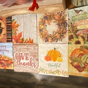 May include: A set of eight fall-themed paper napkins with various designs. The designs include a witch flying on a broomstick, a wreath of fall leaves, a truck with pumpkins, a pumpkin with the word "thankful", a pumpkin with the words "give thanks", a sign with the words "apple orchard", a sign with the words "sunflower field", and a pumpkin with the words "happy thanksgiving".