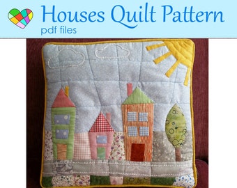 May include: A quilted pillow featuring a patchwork design of colorful houses, a sun, clouds, and a tree against a light blue sky. The pillow has a yellow border and the text "Houses Quilt Pattern pdf files".