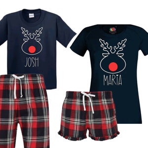 May include: Matching navy blue pajamas with a red-nosed reindeer design. The shirts have the names "Josh" and "Maria" printed on them. The pajamas include plaid shorts.