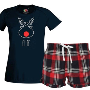 May include: A navy blue t-shirt with a white reindeer design and the name "Ellie" printed on the front. The t-shirt is paired with red and black plaid pajama shorts with a white drawstring.