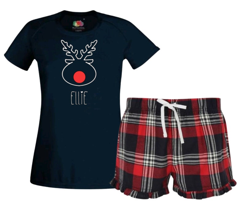 May include: A navy blue t-shirt with a white reindeer design and the name "Ellie" printed on the front. The t-shirt is paired with red and black plaid pajama shorts with a white drawstring.