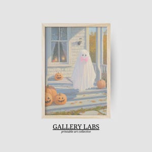 May include: A framed art print featuring a painting of a white ghost wearing a pink bow standing on a porch with orange pumpkins. The porch is attached to a house with a window. The text GALLERY LABS printable art collective is below the image.