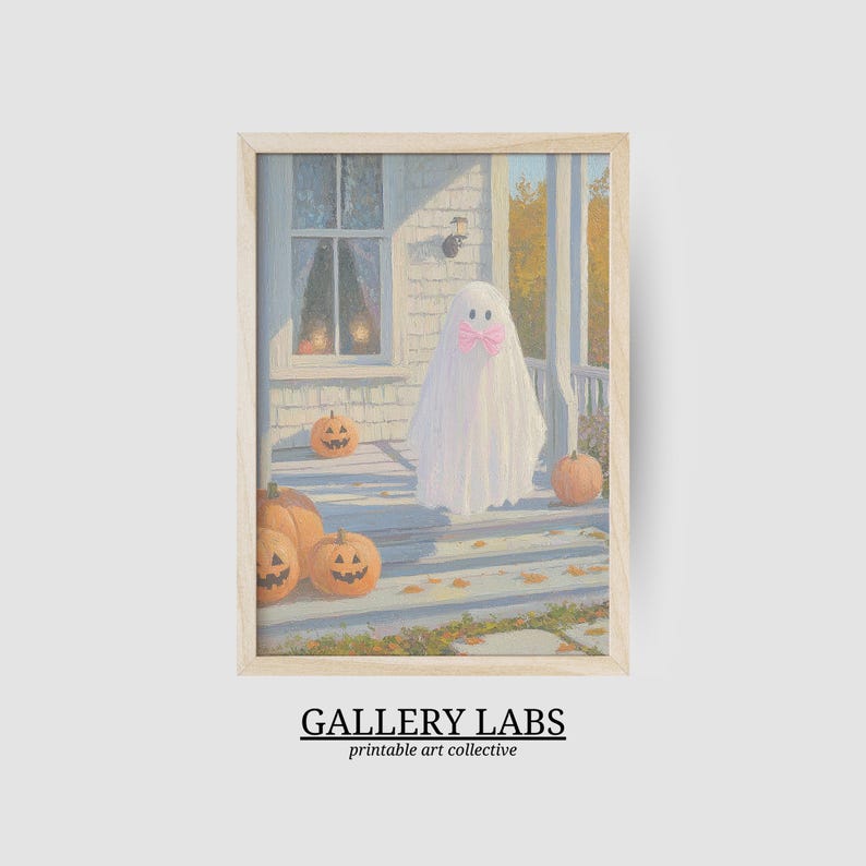 May include: A framed art print featuring a painting of a white ghost wearing a pink bow standing on a porch with orange pumpkins. The porch is attached to a house with a window. The text GALLERY LABS printable art collective is below the image.