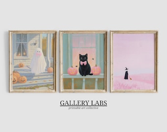 Puede incluir: Tres láminas artísticas enmarcadas con temática de Halloween. La primera muestra un fantasma con un lazo rosa en un porche con calabazas. La segunda representa un gato negro con un lazo rosa y dos calabazas rosas. La tercera muestra una bruja. Texto: GALLERY LABS.