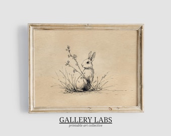 May include: A framed art print featuring a black ink line drawing of a rabbit sitting among tall grasses and wildflowers on a tan background. Below the frame, the text reads GALLERY LABS printable art collective in black capital letters.