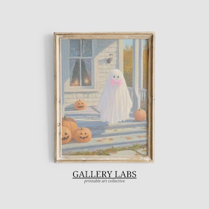 May include: A framed art print depicting a white ghost wearing a pink bow standing on a porch with orange jack-o'-lanterns. The scene features a house exterior with a window and autumn foliage in the background. The text GALLERY LABS is below.
