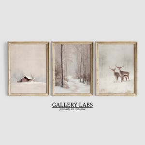 May include: Set of three framed winter landscape prints. The prints depict a snowy barn, a path through a forest, and two deer in a snowy field. The frames are a light wood color. The text "GALLERY LABS printable art collective" is at the bottom.