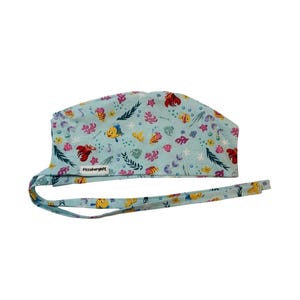 May include: A light blue scrub cap featuring a repeating pattern of colourful cartoon fish, crabs, seashells, and seaweed. The fabric head covering includes long ties for adjustment and a small white rectangular tag labelled PittsburghPE.