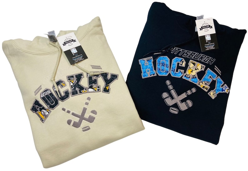 May include: Two hooded sweatshirts with a Pittsburgh Hockey design. One is beige with black and white lettering and the other is navy blue with blue and white lettering.