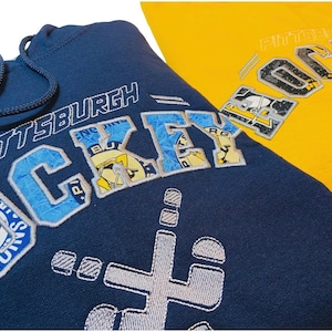 May include: A navy blue hoodie with a white embroidered design that says "Pittsburgh Hockey" with a penguin logo. The hoodie has a drawstring hood and a kangaroo pocket.