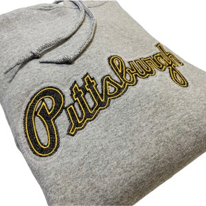 May include: Gray hooded sweatshirt with a black and yellow embroidered "Pittsburgh" logo.