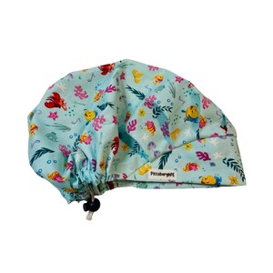 May include: A light blue scrub cap featuring a repeating pattern of colourful cartoon fish, crabs, and coral reef elements. The cap includes a black adjustable toggle cord at the back and a small white fabric tag labelled PittsburghPE.