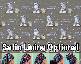 May include: A grey fabric with a repeating pattern of Star Wars characters R2-D2 and Grogu. The fabric has the text "Small but Mighty" repeated throughout. The bottom of the image shows five different styles of surgical caps with the text "Satin Lining Optional" and the names of each style: Euro, Ponytail, Bouffant, Tie Back, and High Bun.