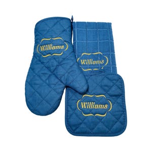 May include: A blue quilted oven mitt, pot holder, and dish towel set. Each item features the name "Williams" embroidered in gold within a decorative frame. The set is designed for kitchen use.