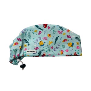 May include: A light blue scrub cap featuring a repeating pattern of yellow fish, pink coral, green seaweed, and bubbles. The fabric cap includes a white rectangular tag with the black text PittsburghPE and a black adjustable cord lock closure.