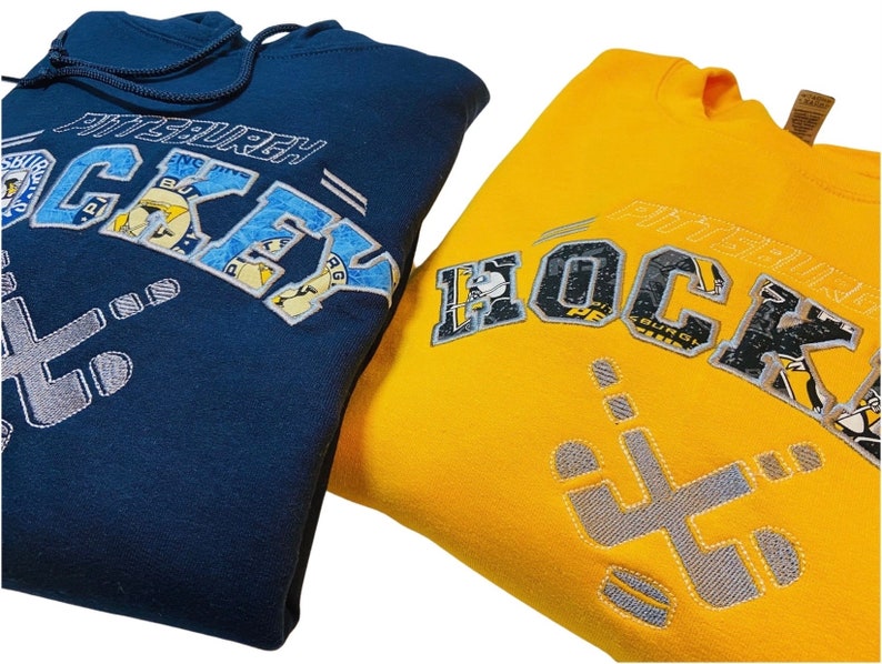 May include: Two sweatshirts, one navy blue and one yellow, with the text "Pittsburgh Hockey" embroidered on the front. The text is made up of smaller patches of fabric with different designs.