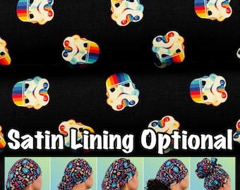 May include: A black fabric with a repeating pattern of rainbow Stormtrooper helmets. The fabric is shown in five different styles of surgical caps: Euro, Ponytail, Bouffant, Tie Back, and High Bun. The text "Satin Lining Optional" is displayed below the fabric.