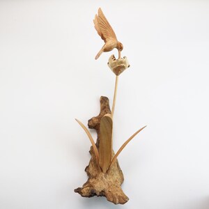 May include: A wooden sculpture of a hummingbird feeding from a flower. The sculpture is made of driftwood and has a natural, rustic look.