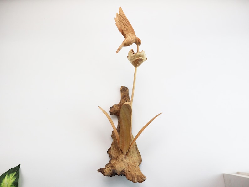 May include: A wooden sculpture of a hummingbird feeding from a flower. The sculpture is made of driftwood and has a natural, rustic look.