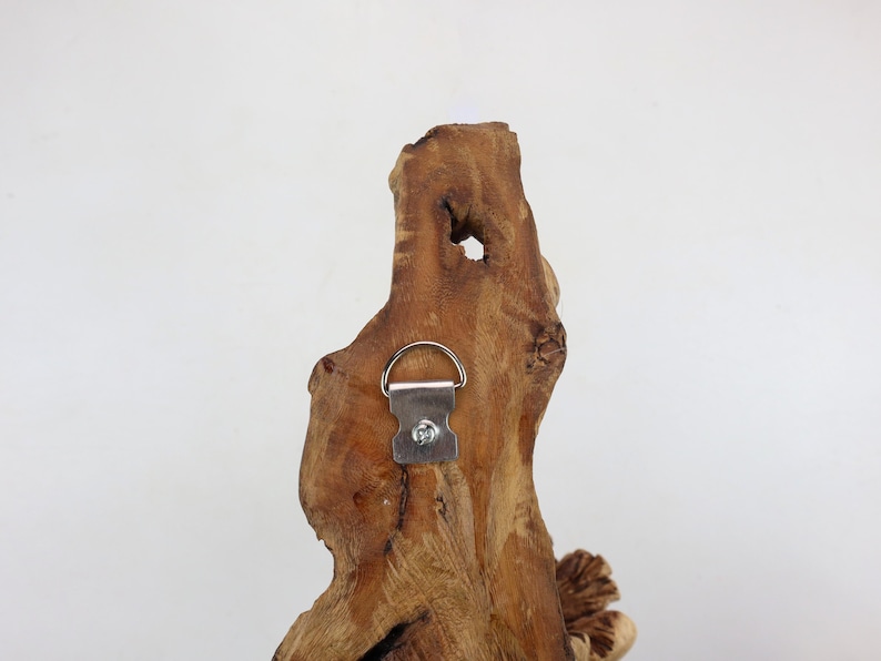May include: A piece of driftwood with a metal hanging hook attached to the back. The wood is a light brown color and has a natural, rustic look.