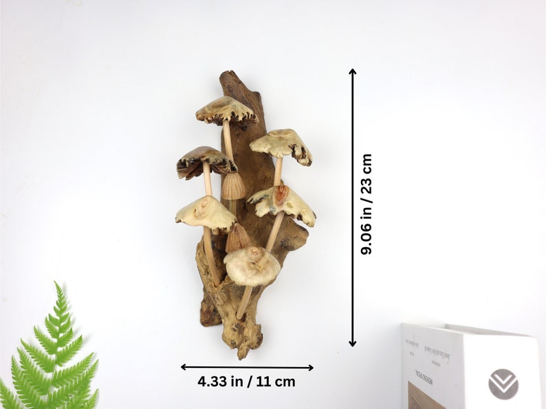 May include: A wooden wall sculpture featuring a cluster of carved mushrooms with brown and beige caps and stems. The sculpture is mounted on a piece of driftwood and measures 9.06 inches tall and 4.33 inches wide.