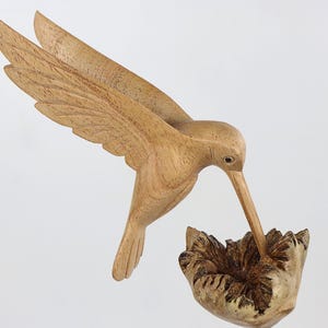 May include: A wooden hummingbird sculpture with its beak in a flower. The sculpture is hand-carved and painted in natural wood tones.