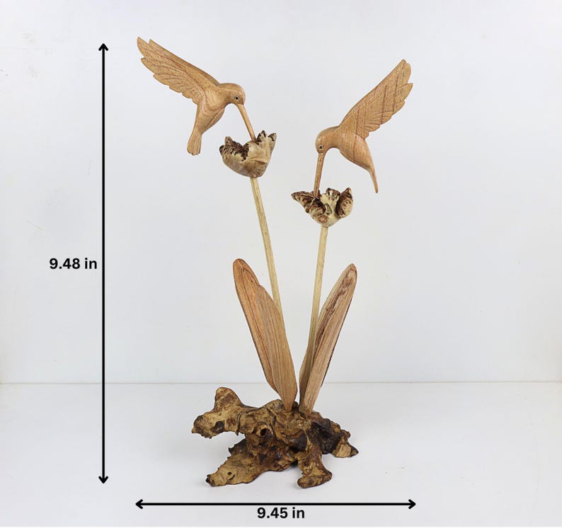May include: A wooden sculpture of two hummingbirds perched on a flower with leaves. The sculpture is made of natural wood and has a rustic finish. It measures 9.48 inches tall and 9.45 inches wide.