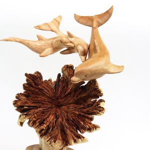 May include: A wooden sculpture of three dolphins leaping out of the water, with a brown wooden base that resembles coral.